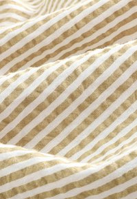 Gestreepte stof met afwisselend dunne witte en beige lijnen, met een zachte, gestructureerde oppervlakte. Het ontwerp is geweven met een natuurlijk, lichtgewicht materiaal.
