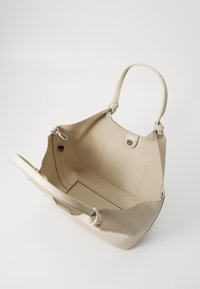 Beige skinnveske med myk, teksturert finish. Har to håndtak og en trykknapplukking. Innvendig med en glidelomme.