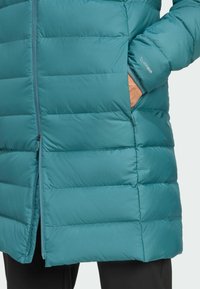 Tirkizna puffer jakna s horizontalnim šavovima, prednjim zipom i bočnim džepovima. Sadrži elastične manžetne s detaljem loga. Glatka, izolirana tkanina.