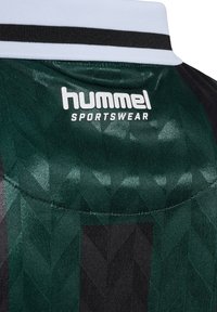 Svart och grön sporttröja med texturerad yta och geometriskt mönster, vit krage och "hummel SPORTSWEAR"-logotyp.