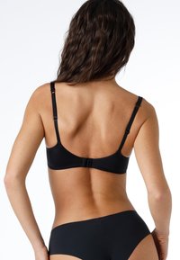 Reggiseno nero con spalline regolabili, tessuto liscio, design curvo nella parte posteriore e chiusura ad gancio. Include anche un coordinato di mutandine nere.
