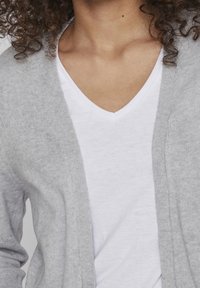 Ljusgrå cardigan i mjukt, stickat material, öppen framsida, tillsammans med en vit t-shirt med v-ringning underneath.