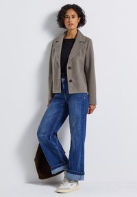Blazer gris ajusté avec revers, deux boutons, associé à un jean bleu large et des baskets blanches. Sac à épaule marron.
