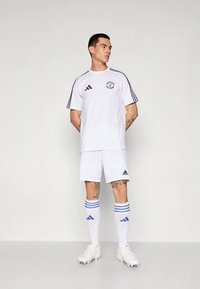 Echipament de fotbal alb format dintr-un tricou cu mânecă scurtă și pantaloni scurți, cu accente dungi albastre pe mâneci și șosete, având un logo Adidas.