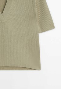 Pull en maille vert clair avec un décolleté en V et des manches courtes, présentant une texture côtelée et une coupe décontractée, légèrement plus long à l'arrière.