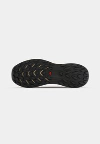 Semelle de chaussure en caoutchouc noir avec des rainures profondes et un petit logo triangulaire rouge au centre, conçue pour la traction et la durabilité.