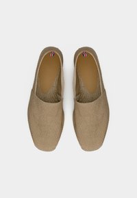 Ζευγάρι μπεζ καμβά slip-on εσπαντρίγιες με καφέ εσωτερικές σόλες και υφασμάτινες λωρίδες κόκκινου, λευκού και μπλε στο τακούνι, σε θέα από πάνω.