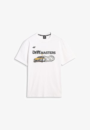Kobieta nosząca białą koszulkę "Drift Masters" z grafiką driftingowego samochodu oraz czarne spodnie typu cargo z naszywkami z logo, stojąca z jedną ręką w kieszeni.