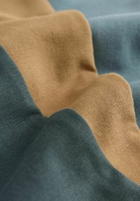 Textil med tre vågiga sektioner i dämpade nyanser: mörkgrön, beige och ljusblå. Mjuk textur med ett ribbat mönster.