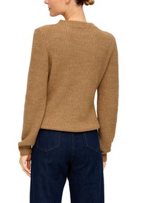 Brauner gestrickter Pullover mit strukturiertem Muster, Rundhalsausschnitt und gerippten Bündchen, kombiniert mit dunkelblauen Jeans.