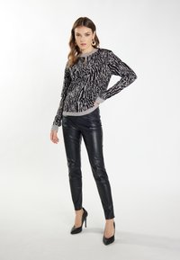 Zwart-wit gemusterde gebreide trui met een ronde hals, grijze ribgebreide manchetten, gecombineerd met glanzende zwarte leren broeken en zwarte high heels.