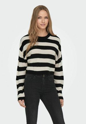 Maglione cropped a righe bianche e nere con maniche lunghe, texture in maglia e scollatura rotonda, abbinato a jeans neri.