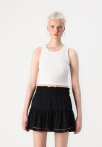 Hvit perlestrikket crop top sammen med et svart lagdelt skjørt med smock-bredde og blondekant, plassert mot en enkel hvit bakgrunn.