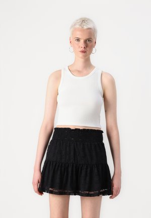 Hvit perlestrikket crop top sammen med et svart lagdelt skjørt med smock-bredde og blondekant, plassert mot en enkel hvit bakgrunn.