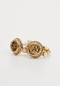 Bague en métal doré avec un design floral découpé complexe, entourée de pierres transparentes et accentuée de petites perles blanches. Forme circulaire, finition texturée.