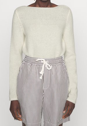 Personne portant un pull duveteux crème clair et un short rayé vertical noir et blanc taille haute avec une ceinture blanche à cordon.