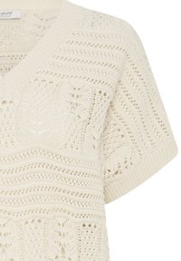 Krém színű kötött pulóver V-nyakkal, rövid ujjal és aprólékos, nyitott mintázattal, hullámos és levélszerű mintákkal az egész felületen.