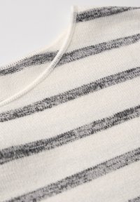 Gestreepte gebreide top met horizontale grijze en witte strepen, een gladde textuur en een ronde halslijn. Close-up van de stikseldetails.