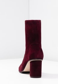 Botines de ante burdeos con tacón de bloque, que presentan una textura suave, un diseño ajustado y una parte trasera sin costuras ni herrajes visibles.