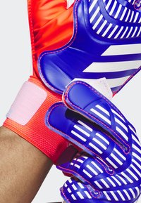 Guanti da portiere con un design blu e bianco, caratterizzati da una presa testurizzata, dita rinforzate e un cinturino da polso rosso regolabile.