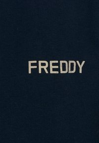 Camiseta de algodón azul marino con la palabra "FREDDY" en letras blancas y en bloque. La tela tiene una textura suave sin patrones visibles.