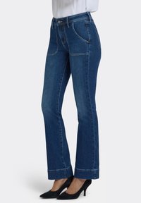 Jeans acampanados de mezclilla azul con dos bolsillos delanteros, cintura alta y costuras en contraste. La tela tiene una textura suave con un ligero estiramiento.