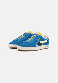 Modré semišové tenisky s žlutými akcenty, bílým lemováním a texturovanou gumovou podrážkou. Obsahují klasické logo PUMA a dekorativní prošívání.