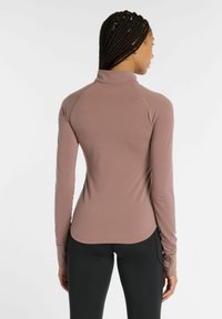 Maglietta atletica a maniche lunghe e colletto alto in tessuto malva. Presenta un design aderente, una texture liscia e aperture per il pollice nei polsini.