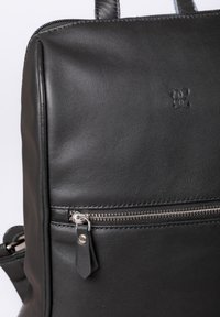 Black leather backpack featuring a smooth texture, zippered front pocket, and embossed logo. Structured design with durable handles.