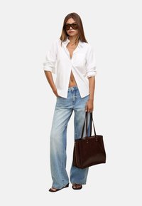 Camicia bianca con maniche arrotolate, jeans a gamba larga blu chiaro e una borsa a tracolla marrone scuro. Occhiali da sole oversize completano il look.