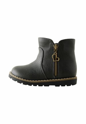 Bottine en cuir noir avec fermeture éclair latérale dotée d'une tirette en forme de cœur et semelle épaisse à crampons avec surpiqûres beiges.