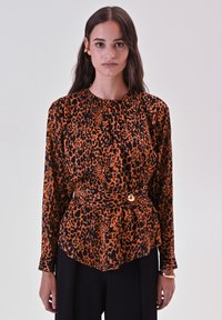 Blusa con stampa leopardata in arancione e nero, maniche lunghe, scollatura arricciata, vita cinte con un accento dorato. Abbinata a pantaloni neri.