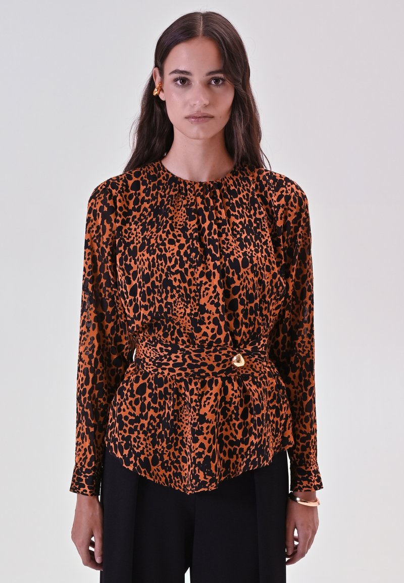 Blusa con stampa leopardata in arancione e nero, maniche lunghe, scollatura arricciata, vita cinte con un accento dorato. Abbinata a pantaloni neri.