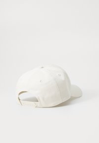 White cotton baseball cap with a curved brim, adjustable snapback closure, and six ventilated eyelets on the crown. Minimalist design.
