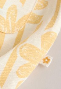 Bavlnená látka so žltým kvetinovým a pruhovaným vzorom. Má textúrovaný povrch a malú štítok s detailom kvetu.