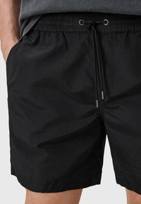 Costumi da bagno neri realizzati in tessuto leggero, con vita elasticizzata e lacci, tasche laterali e una superficie liscia.