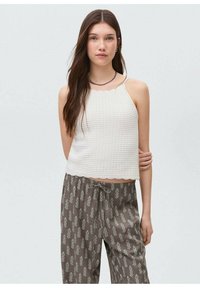 White, textured crop top with scalloped hem; paired with brown, drawstring pants featuring a leaf pattern. Solid straps on the top.