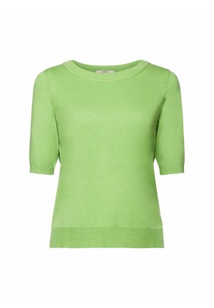 Femme portant un haut en maille à manches courtes vert clair associé à un pantalon blanc taille haute noué avec une ceinture en tissu.