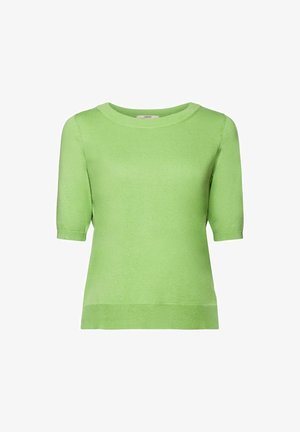 Mujer vistiendo un top de punto de manga corta color verde claro combinado con pantalones blancos de cintura alta atados con un cinturón de tela.