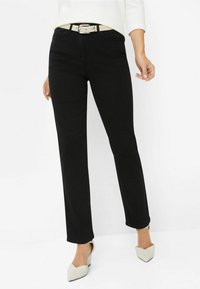 Jeans neri a gamba dritta con una texture liscia, dotati di tasche frontali e una cintura beige con una fibbia in argento. Indossati con scarpe chiare a punta.