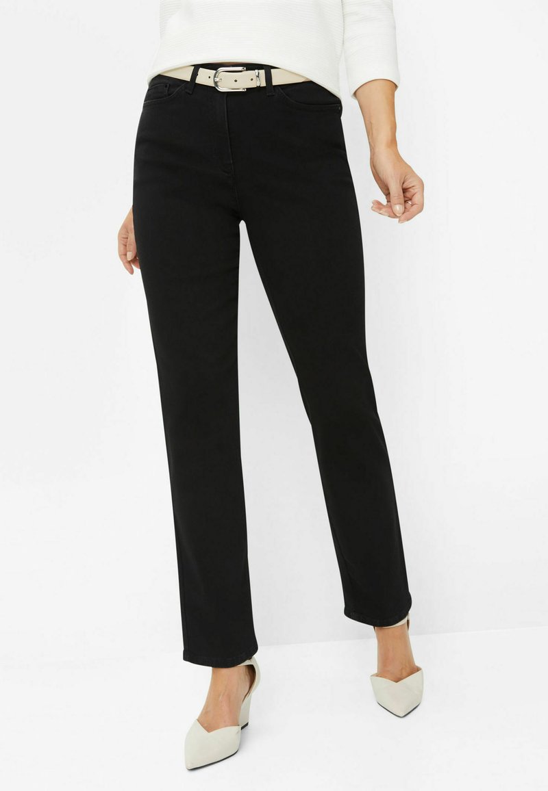 Jeans neri a gamba dritta con una texture liscia, dotati di tasche frontali e una cintura beige con una fibbia in argento. Indossati con scarpe chiare a punta.