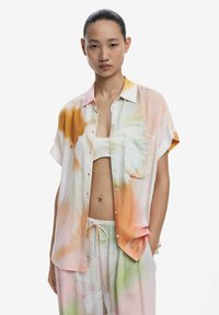 Košeľa s krátkym rukávom s kvetinovým akvarelovým vzorom v pastelových farbách. Vyrobená z ľahkej tkaniny, s náprsné vreckom a voľným strihom.