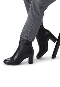 Bottines en cuir noir avec une finition lisse, un bout arrondi et un talon carré. Présentent un design froncé au niveau de la cheville et une fermeture éclair latérale.