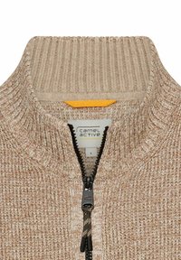 Beige Strickpullover mit hohem Kragen, ausgestattet mit einem Viertel-Reißverschluss an der Vorderseite, strukturiertem Stoff und einem kontrastierenden gelben Akzent in der Nähe des Etiketts.
