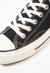 Baskets en toile noire avec lacets blancs, bout en caoutchouc blanc et semelle en caoutchouc blanc avec bande noire, vues en gros plan.