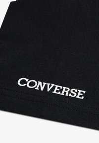 Μαύρο ύφασμα με ομαλή υφή και το λευκό λογότυπο "CONVERSE"  εμφανίζεται έντονα κοντά στην κάτω άκρη. Απλός, μινιμαλιστικός σχεδιασμός.