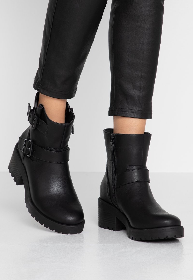 Svarta läderankelstövlar med dubbla spännen, siddragkedja, stabil blockklack och texturerad gummisula. Glatt yta med strukturerad design.