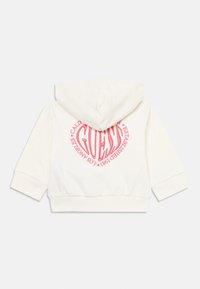White cropped hoodie made of soft fabric featuring a large round pink logo on the back with "GUESS" and establishment details.