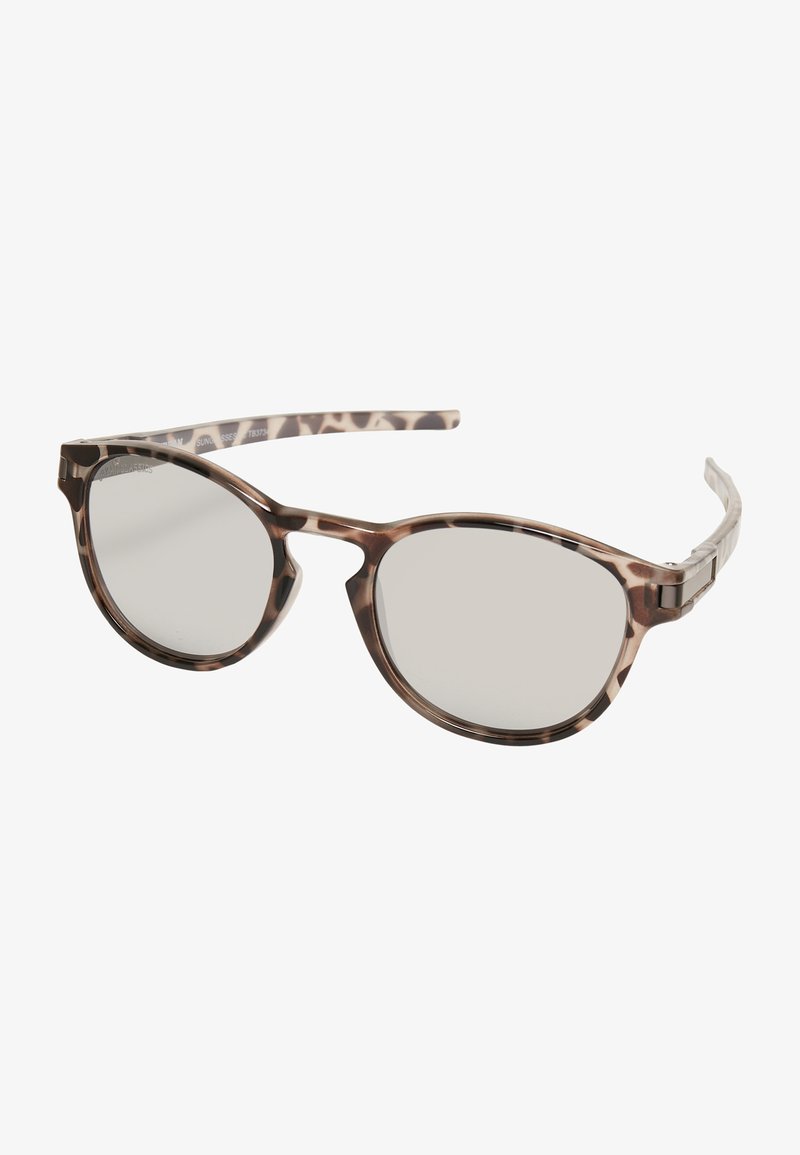 Pruunile täkilised päikeseprillid ümarate läätsedega, õhukeste sanga ja siledast plastist raami. Läätsed on veidi peegeldavad ja peegeldavad.