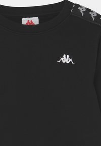 Sweat-shirt noir avec col côtelé. Présente un logo brodé blanc sur la poitrine et des accents à motifs sur les épaules. Texture douce.